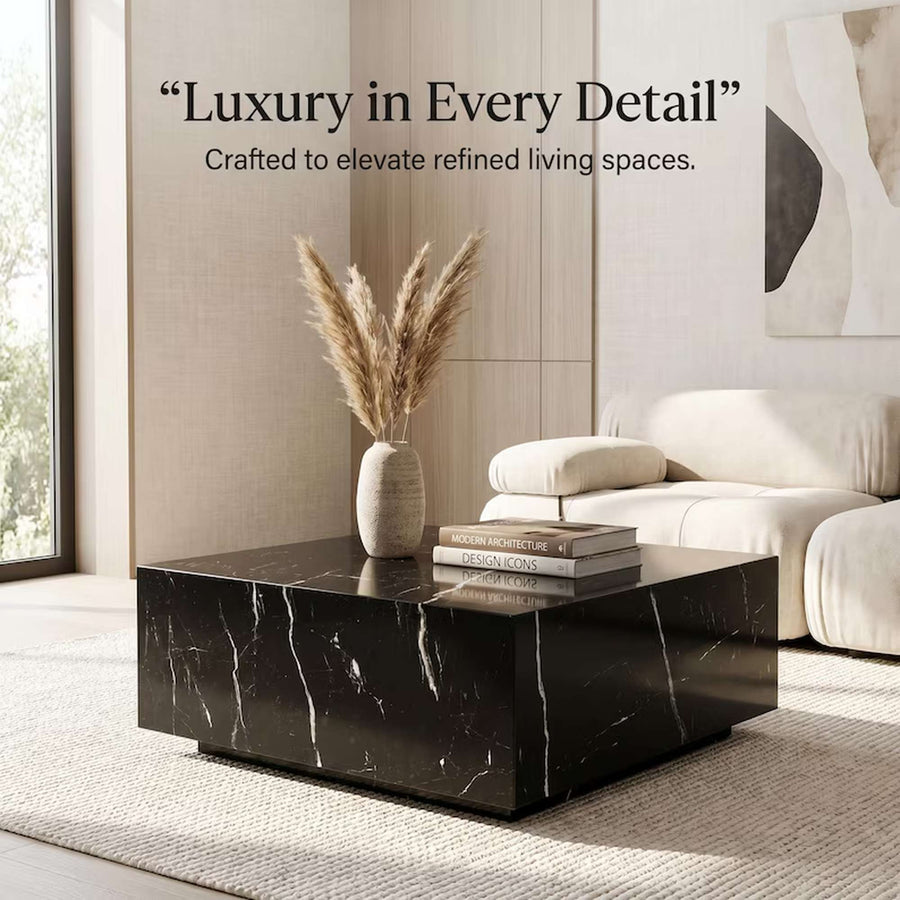 A modern square black marble coffee table with white veining, styled in a minimalist living room with a beige sofa, a vase of pampas grass, and stacked books on top. Text overlay reads: 'Luxury in Every Detail' and 'Crafted to elevate refined living spaces.