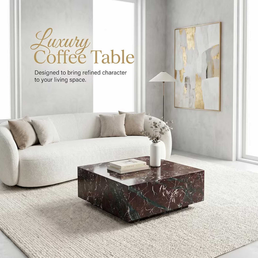 A luxury coffee table made of dark brown and black marble with green veining, styled in a modern living room setting with a cream sofa, beige rug, and a gold-framed abstract painting on the wall.