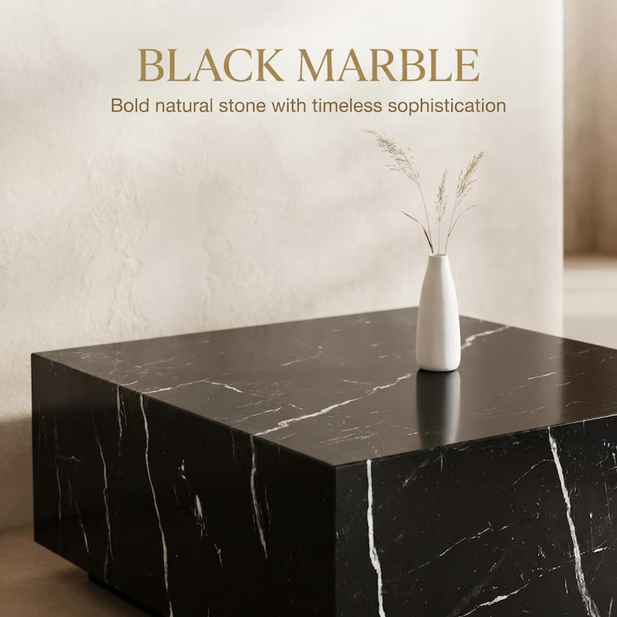 A black marble side table with white veining, styled with a small white vase containing dried grasses, set against a textured beige wall with the text 'BLACK MARBLE Bold natural stone with timeless sophistication'.