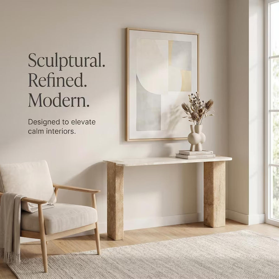 A styled interior scene with a light wood console table, framed abstract wall art, a cream chair, rug, and dried floral arrangement in a vase. Large text on the left reads, 'Sculptural.