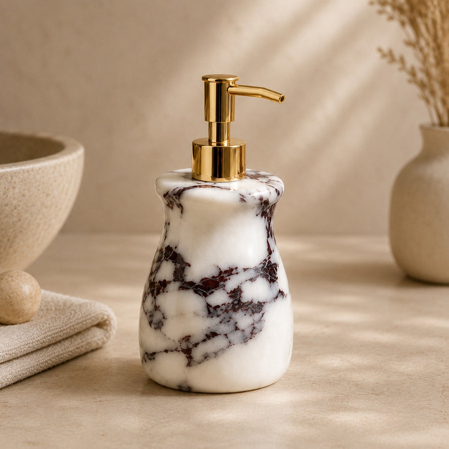 A marble soap dispenser with a white and dark gray veined pattern and a shiny gold pump, set on a beige surface with a neutral background.