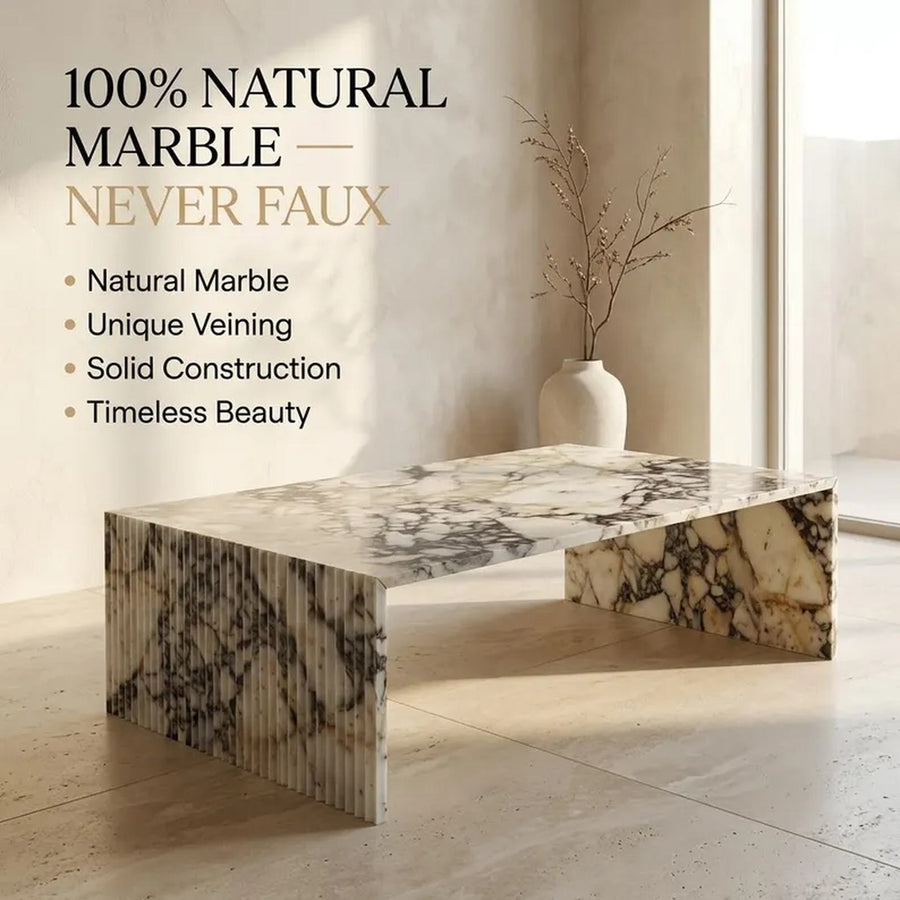 A rectangular marble coffee table with fluted legs and a thick marble top, shown in a minimalist interior setting with text on the left reading '100% NATURAL MARBLE — NEVER FAUX'.