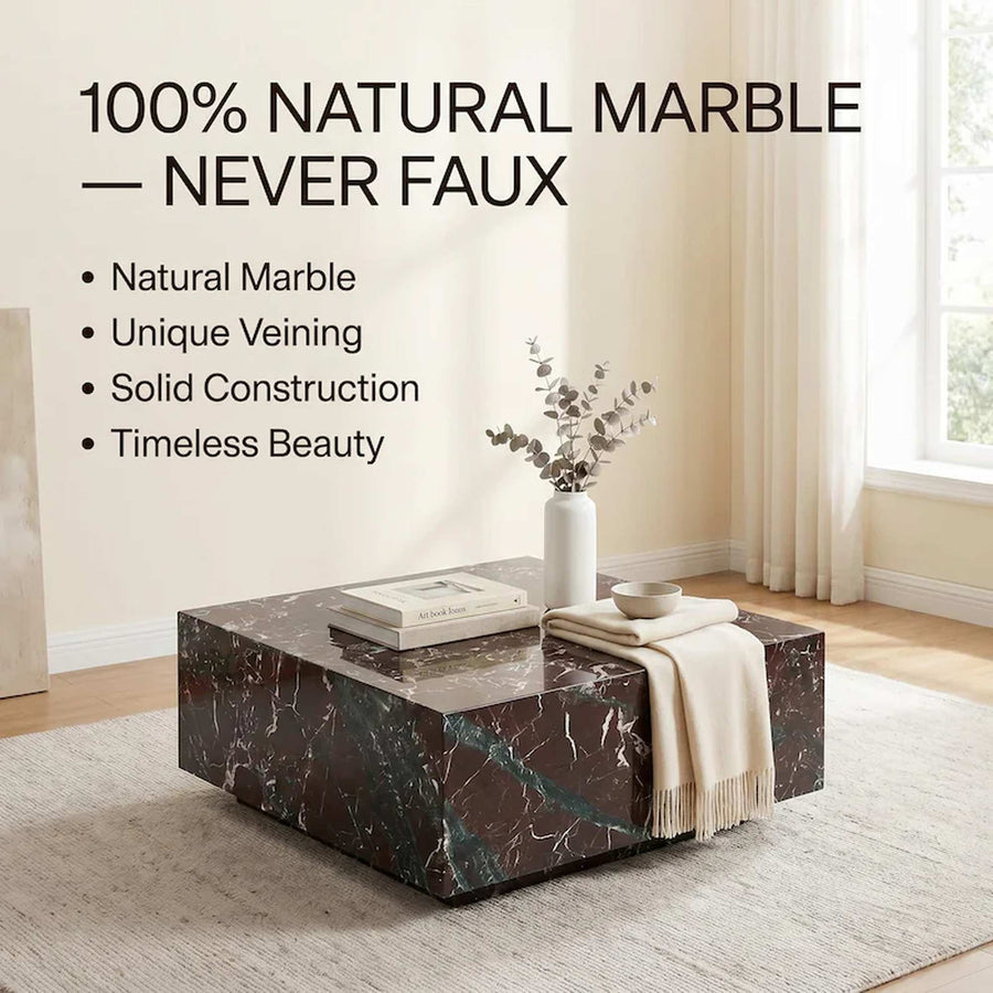 A rectangular coffee table made of dark natural marble with white and green veining, styled in a bright living room with a vase, books, and a throw blanket. Text on the left reads '100% NATURAL MARBLE — NEVER FAUX' with bullet points highlighting natural marble, unique veining, solid construction, and timeless beauty.