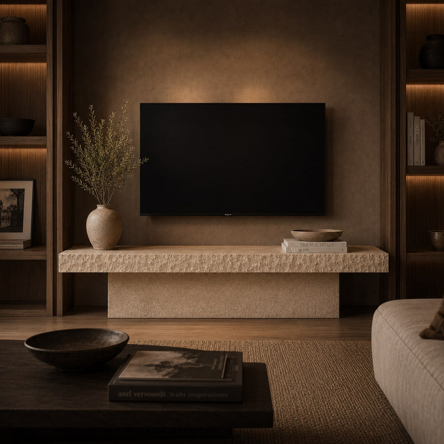 A modern living room scene featuring a black flat-screen TV mounted on a textured brown wall above a stone console. The room has warm ambient lighting, built-in wooden shelving with backlit books, a beige sofa edge, and a dark coffee table in the foreground.