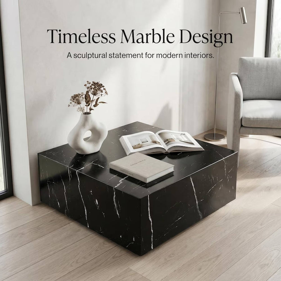 A modern black marble coffee table with white veining, styled with a white vase, dried flowers, and an open book in a minimalist living room setting. Text overlay reads 'Timeless Marble Design'.