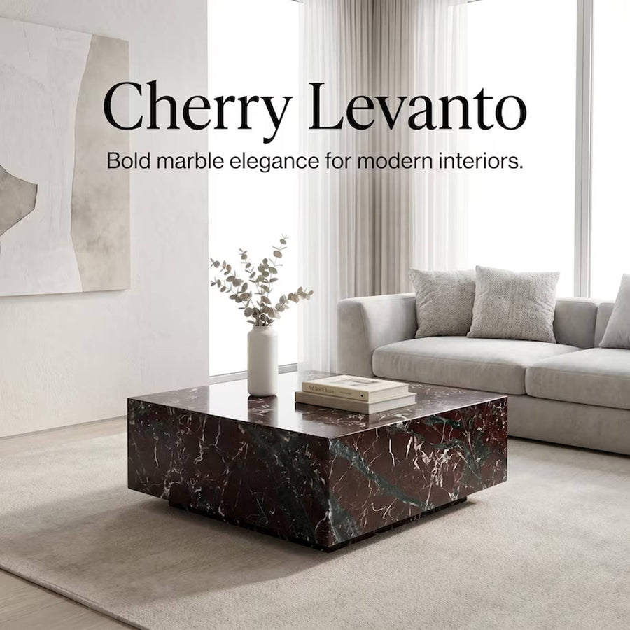 A modern living room scene featuring a dark cherry levanto marble coffee table in the foreground, with a light gray sofa and large windows in the background. Text overlay reads 'Cherry Levanto Bold marble elegance for modern interiors.