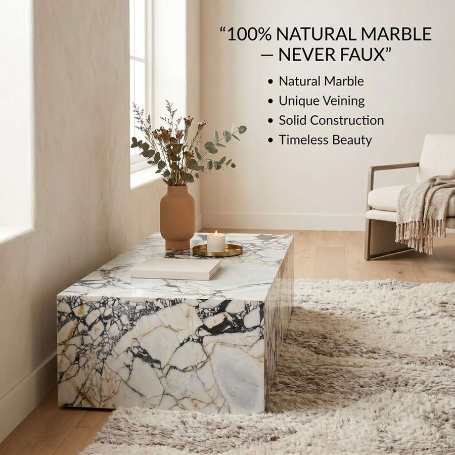 A rectangular coffee table made of natural marble with dramatic black, gray, and gold veining on a white base, styled in a bright living room with a vase, candle, rug, and chair. Text on the image reads: “100% NATURAL MARBLE — NEVER FAUX” with bullet points.
