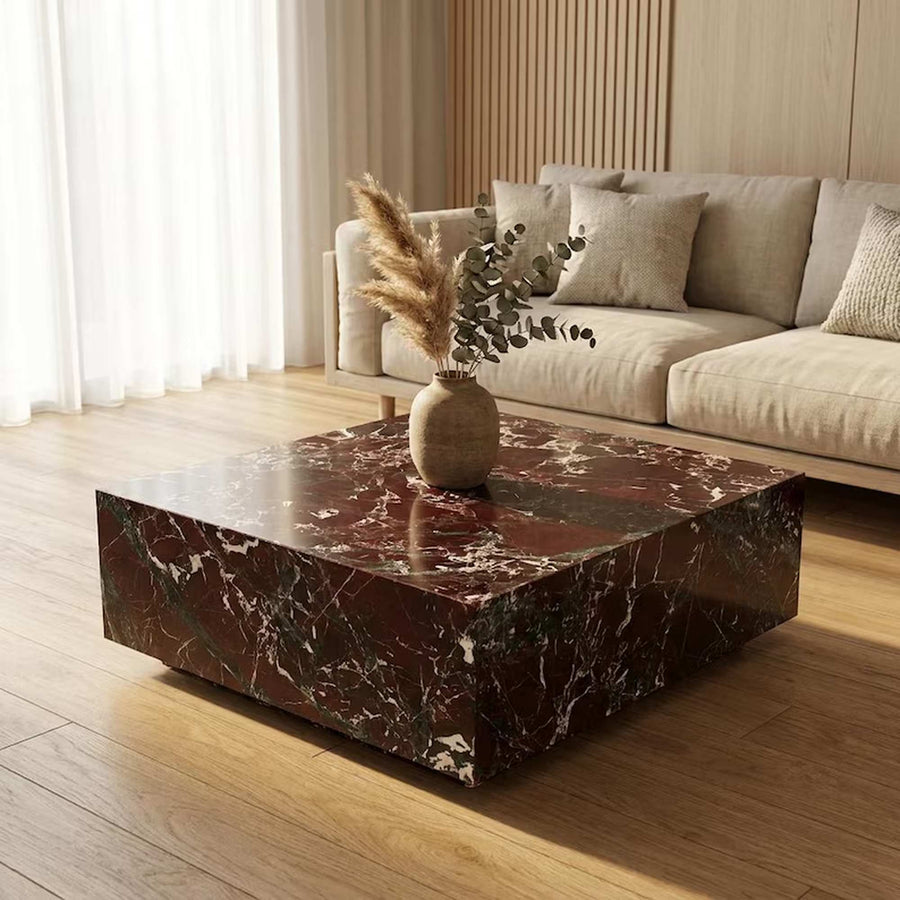 A square coffee table with a glossy dark red-brown marble top and matching base, styled in a modern living room with a beige sofa and wooden floor.