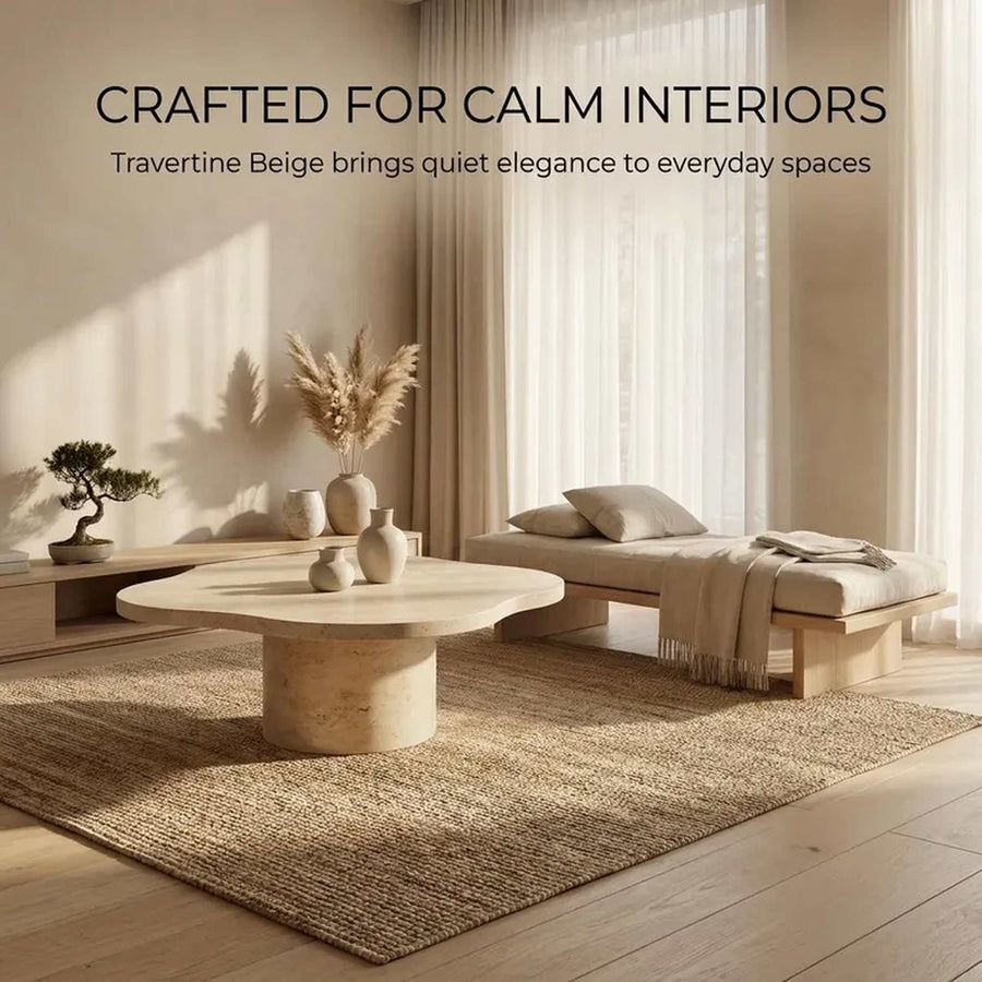 A styled interior scene with a travertine beige round coffee table in the foreground, a matching woven rug, a light wood daybed with cushions and throw, curtains, and warm sunlight. Text at the top reads: 'CRAFTED FOR CALM INTERIORS' and 'Travertine Beige brings quiet elegance to everyday spaces.