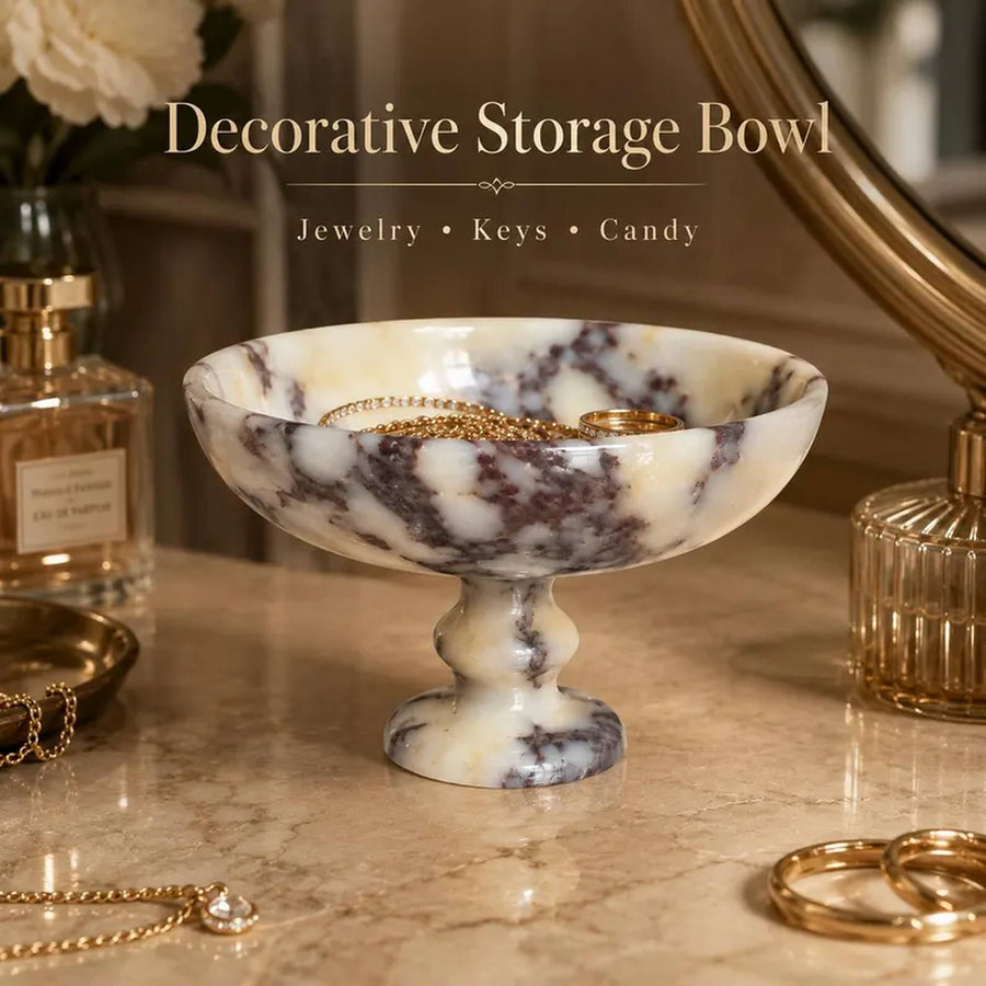 A decorative pedestal storage bowl made of cream and dark gray marbled stone, styled on a marble tabletop with jewelry and keys inside the bowl. Text overlay at the top reads 'Decorative Storage Bowl' with 'Jewelry • Keys • Candy' below.