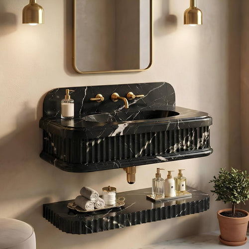 A modern floating bathroom vanity made of black marble with white veining, featuring a fluted front, integrated sink, and gold-tone faucet hardware. A matching marble shelf sits below, styled with toiletries, and the scene is lit by warm wall sconces with a mirror above.