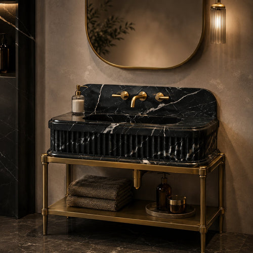 A luxury bathroom vanity featuring a black marble sink with white veining and a ribbed front, mounted on a gold metal stand. The setup includes a gold faucet, matching gold wall-mounted mirror, and warm ambient lighting against a textured beige wall.