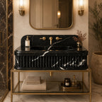 A luxury bathroom vanity featuring a black marble sink with white veining, mounted on a gold metal frame. The setup includes a gold wall mirror, gold sconces, beige towels, and decorative items on a marble floor.