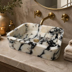 Wall-mounted black and white marble sink under an oval mirror with a woven basket below