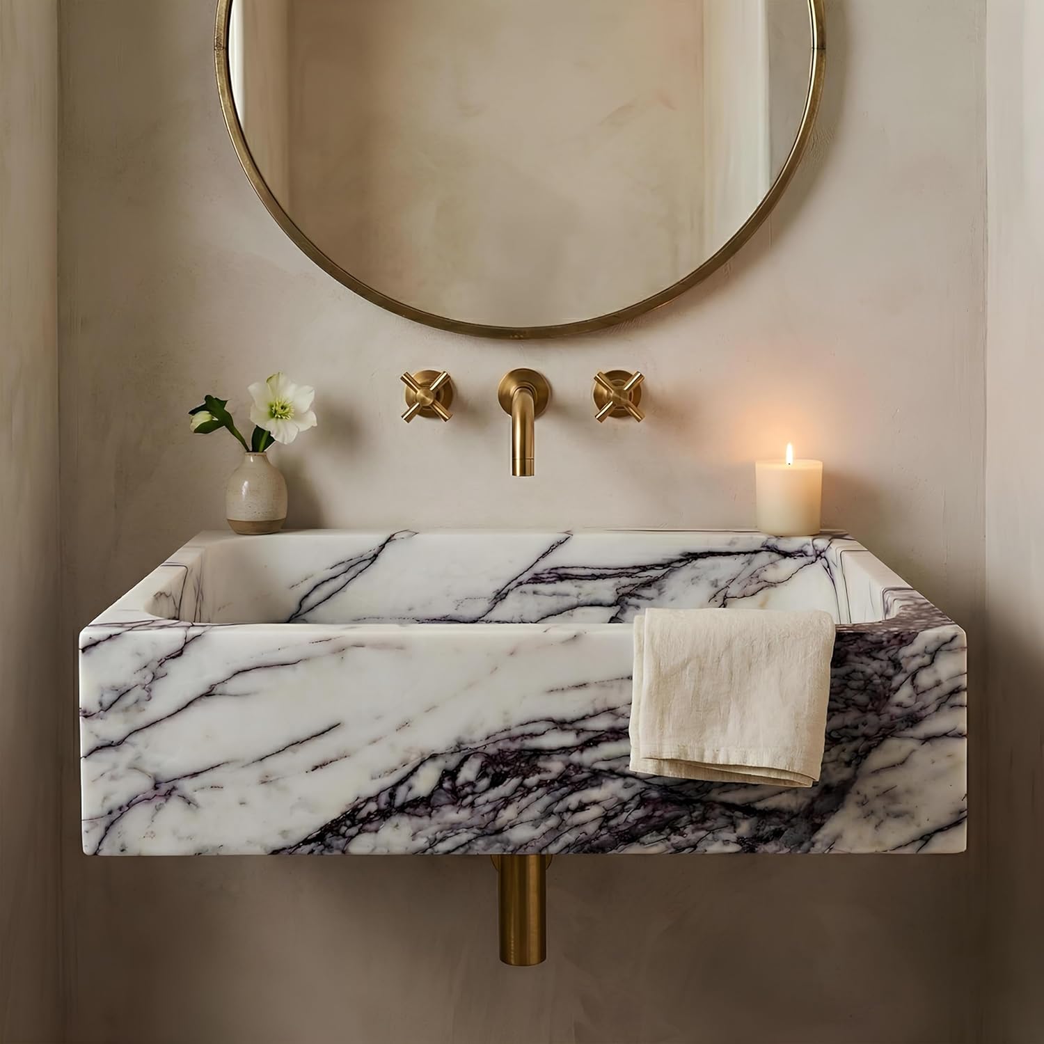 Marble sink with gold fixtures and a round mirror on a beige wall.