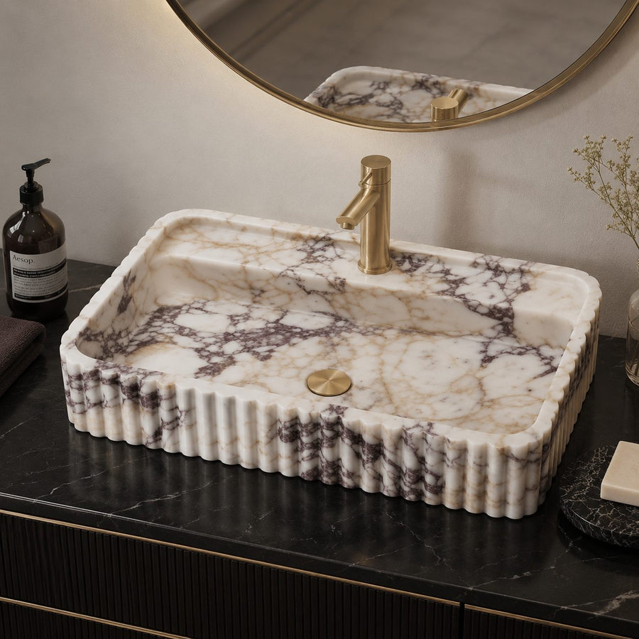 Calacatta Viola marble sink on a black marble countertop with brass faucet