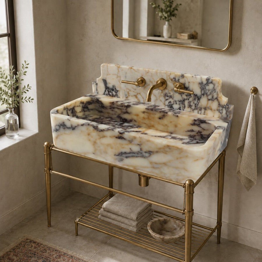 A marble-look rectangular vessel sink with cream, beige, and dark blue-gray veining, mounted on a brass metal stand in a bathroom setting.