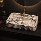 Calacatta Viola marble sink on a black marble countertop with brass faucet