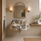 A floating vanity sink with a black-and-white marble pattern and pleated front, installed in a beige bathroom with a matching marble mirror, gold wall sconces, and a wooden shelf with a vase.