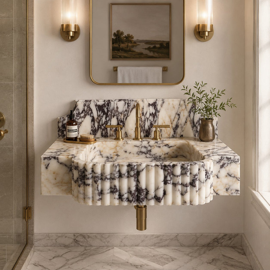 A luxury wall-mounted bathroom sink made of fluted white marble with dramatic black veining, paired with a matching marble backsplash and gold-finished fixtures, set in a beautifully styled bathroom.