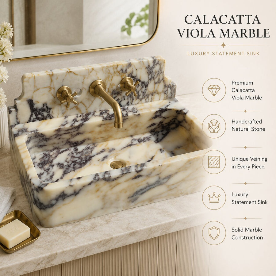 A luxury statement sink made of Calacatta Viola Marble with a warm cream and beige base and dark brown to black veining, paired with a brushed brass faucet and handles. The sink is mounted on a matching marble countertop with a soap dish.