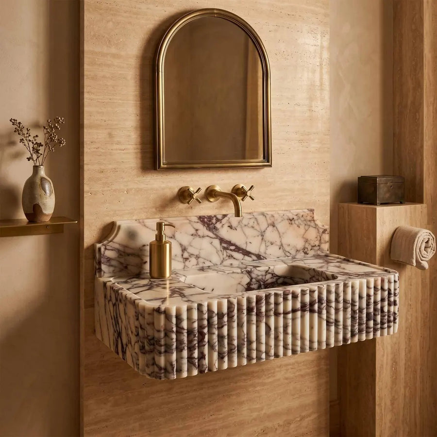 A floating bathroom sink made of fluted marble with a cream and gray veined pattern, mounted on a beige stone wall. The sink has a matching marble backsplash and a ribbed fluted front.