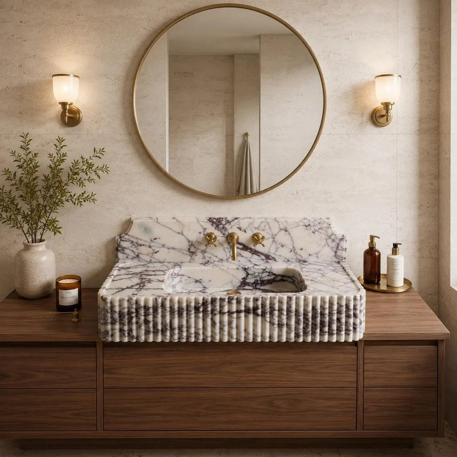 A luxury bathroom vanity setup featuring a rectangular white marble sink with dramatic black veining, set into a dark wood cabinet. The sink is topped with a ribbed, pleated marble front.