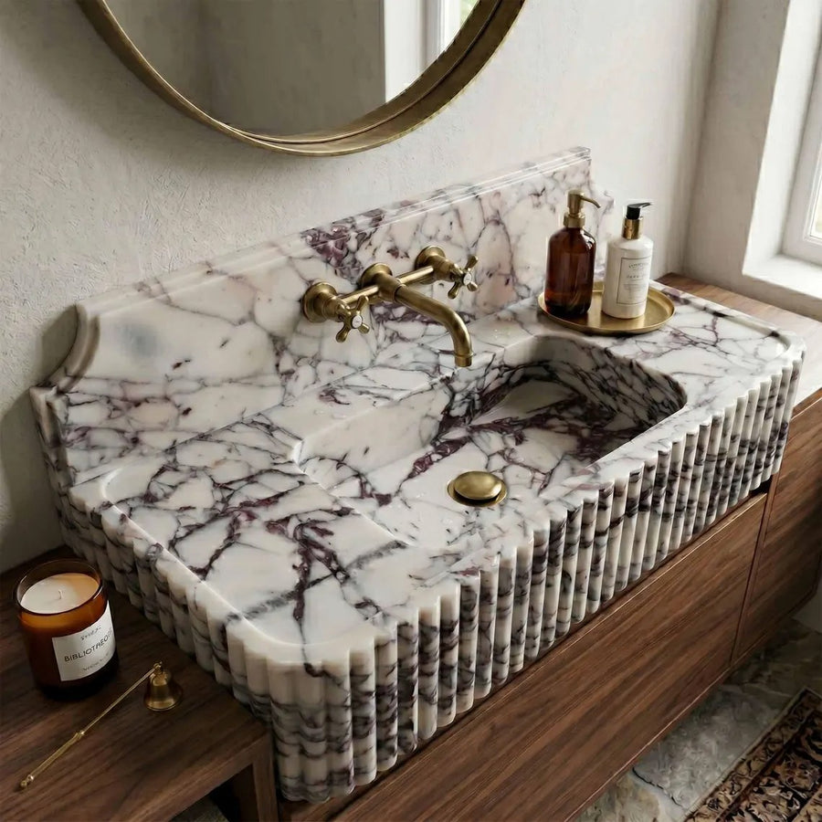 A luxury marble sink vanity with a fluted front, featuring a white and gray veined marble countertop and basin, paired with a brass faucet and gold-toned accessories on a wooden cabinet.
