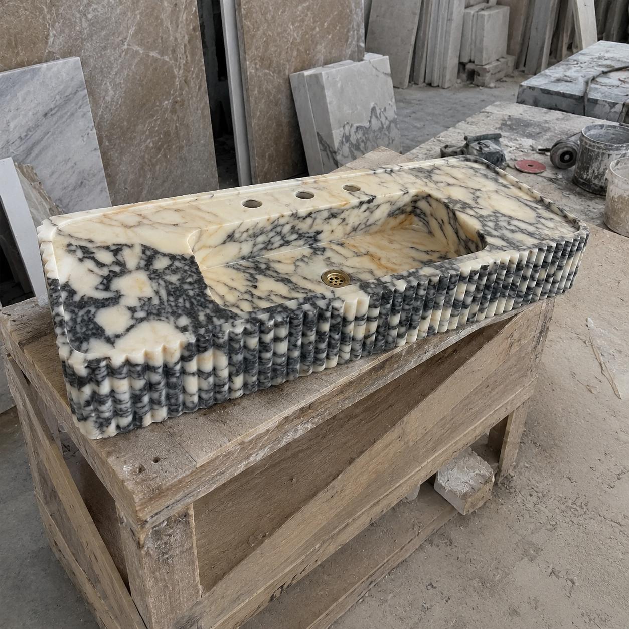 A rectangular carved stone basin with a cream, black, and gray marbled pattern, displayed on a wooden crate in a workshop setting.