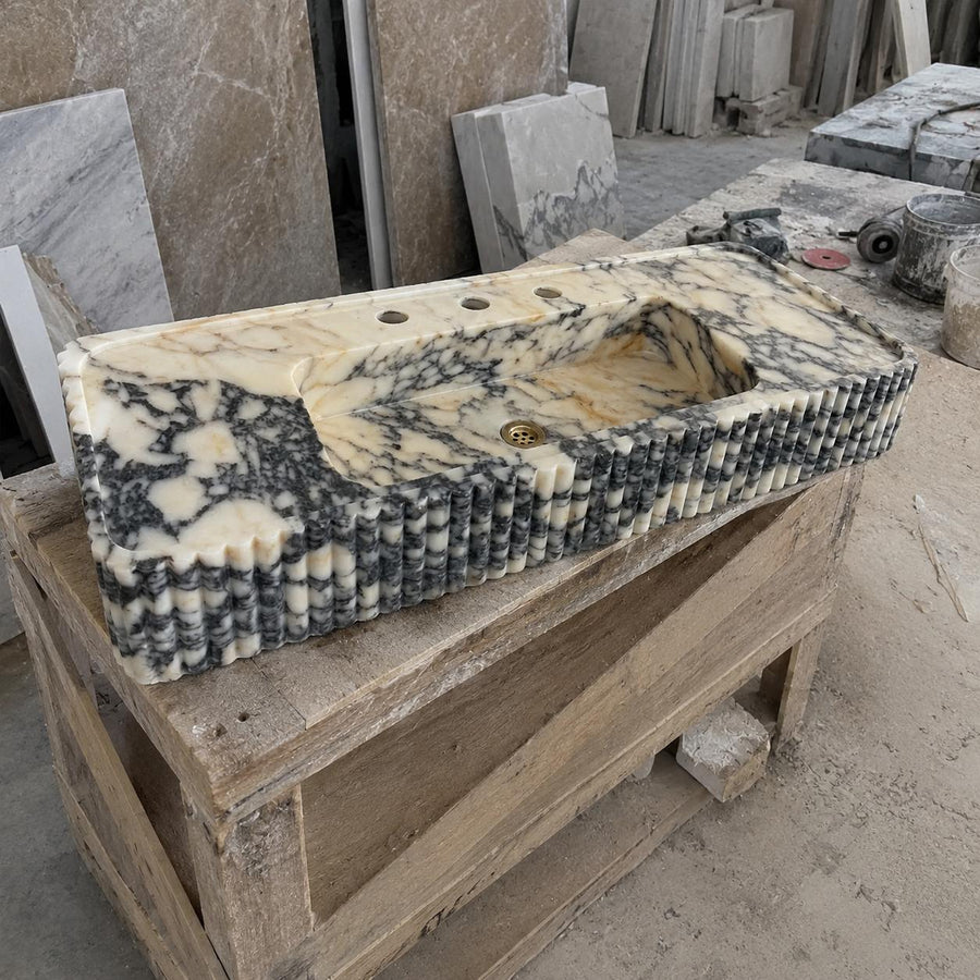 A rectangular carved stone basin with a cream, black, and gray marbled pattern, displayed on a wooden crate in a workshop setting.