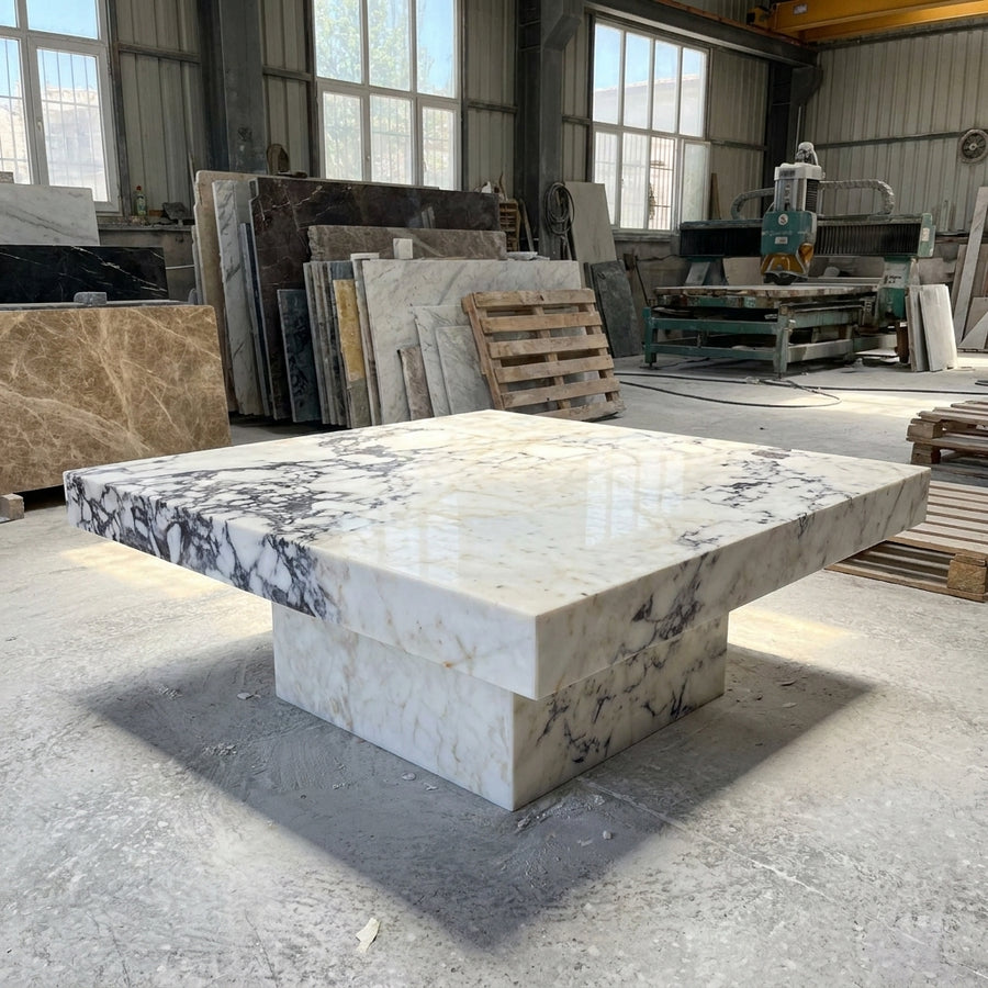 Marble-patterned stone table in a warehouse setting with various stone slabs and equipment.