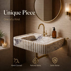 A wall-mounted rectangular stone sink with a fluted front, white marble-like surface, and dark veining, shown in a bathroom setting with a gold faucet, round mirror, and warm ambient lighting. Text on the image reads 'Unique Piece One of a Kind' with feature icons below.