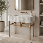 A freestanding rectangular bathroom sink with a white marble-look ribbed front, supported by ornate brass legs and matching brass faucet hardware, shown in a styled bathroom setting with a mirror, plant, and shelving.