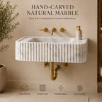 A wall-mounted rectangular sink made of natural marble with a fluted front and polished basin, shown with brass faucet hardware and a small soap dispenser against a beige wall. Text above reads 'HAND-CARVED NATURAL MARBLE' and icons below highlight solid marble, fluted front, polished basin, and one-of-a-kind quality.