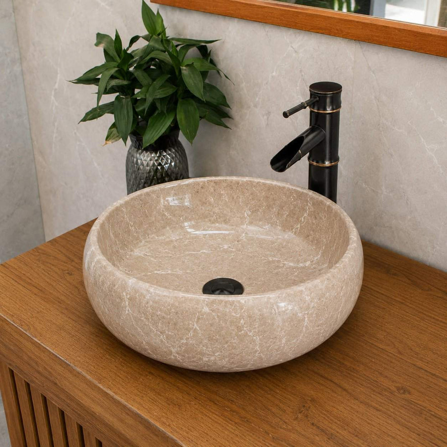 Beige stone sink on a wooden cabinet with a black faucet and green plant in the background.
