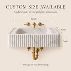 A wall-mounted rectangular sink with a white marble-look front, fluted vertical detailing, and gold faucet hardware on a beige background. Text at the top says 'CUSTOM SIZE AVAILABLE' with arrows labeling length, width, and depth, and additional text stating the sink is made to order.