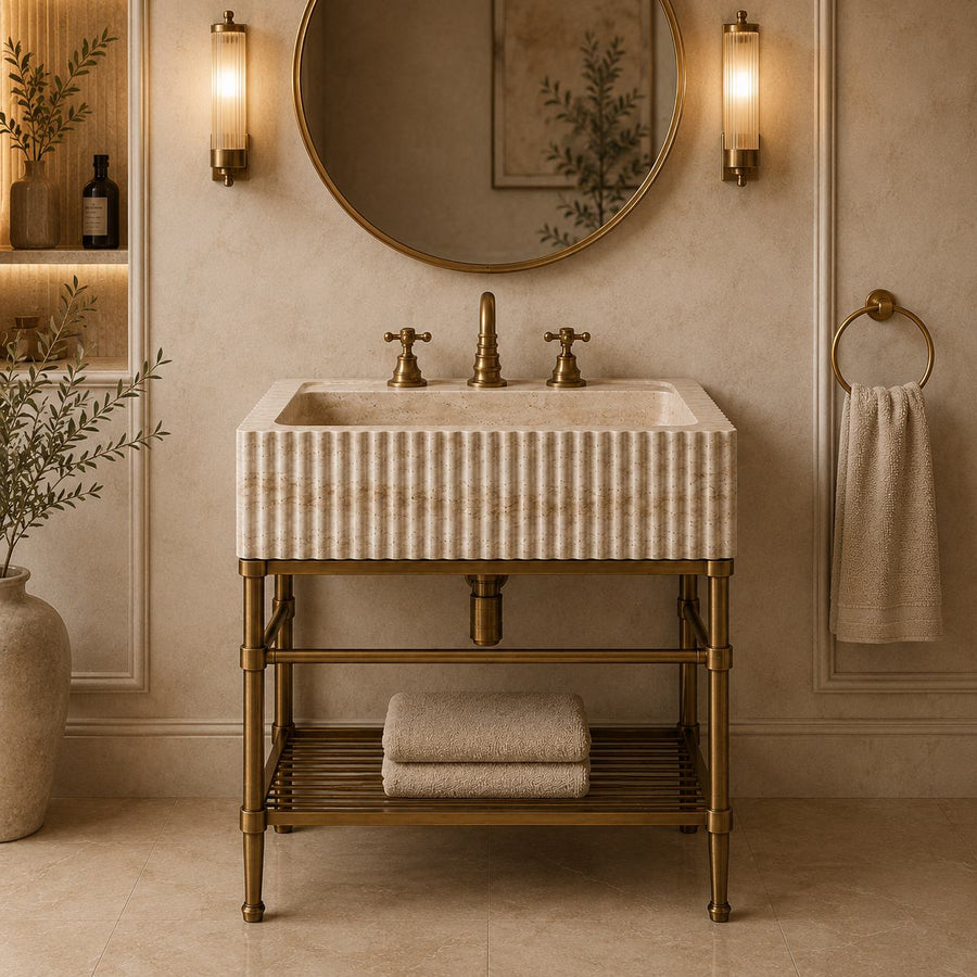 Fluted travertine sink on a brass console in a beige paneled bathroom with round mirror