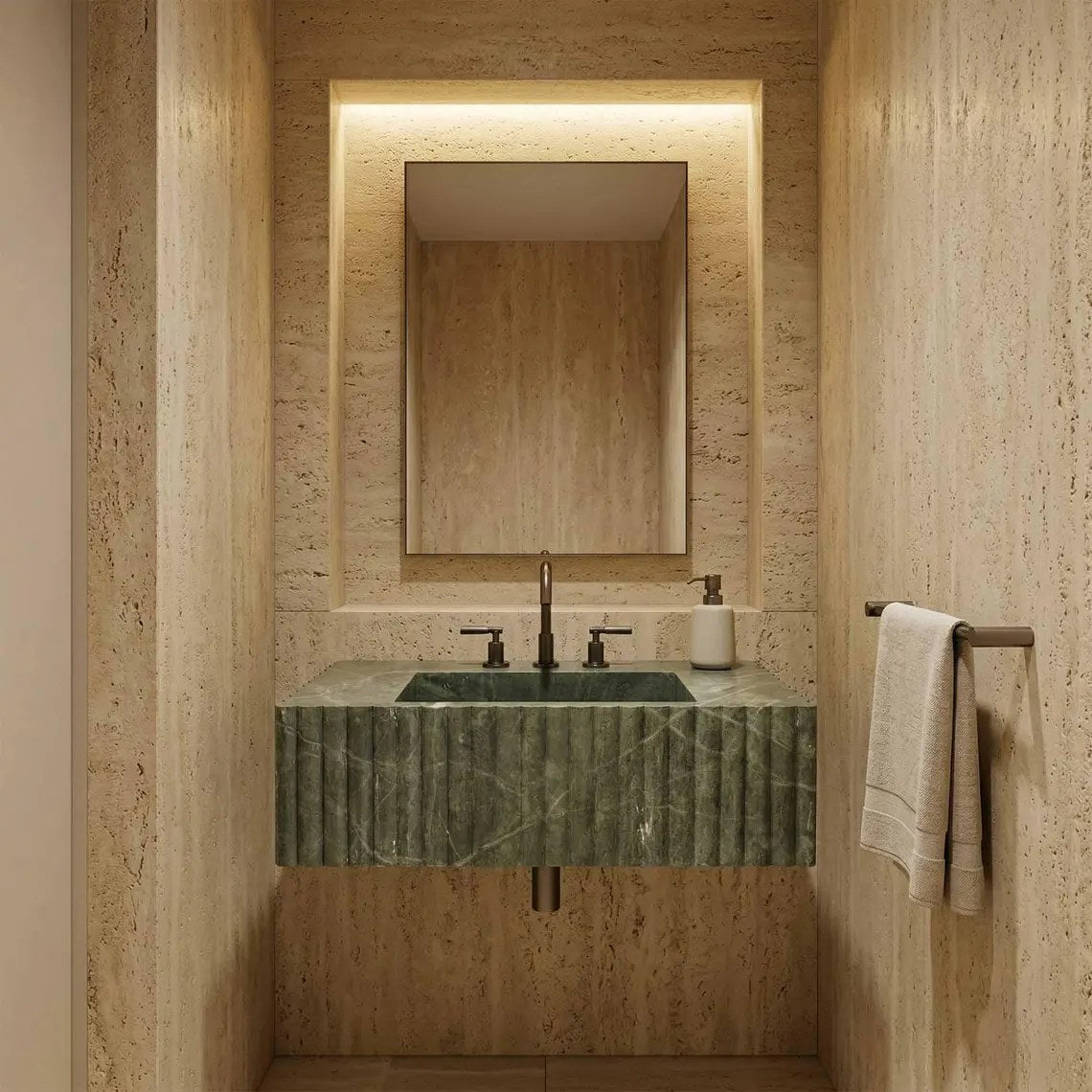 A modern bathroom vanity featuring a green marble sink with a fluted front, set against a warm beige travertine stone wall. A matching rectangular mirror is mounted above, with a black faucet and a white soap dispenser.