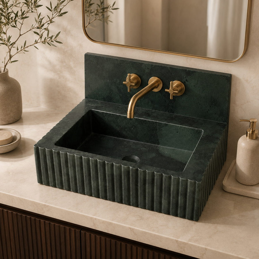 A dark green fluted stone sink with a matching rectangular basin and a brushed brass faucet, installed on a light marble countertop in a bathroom setting.