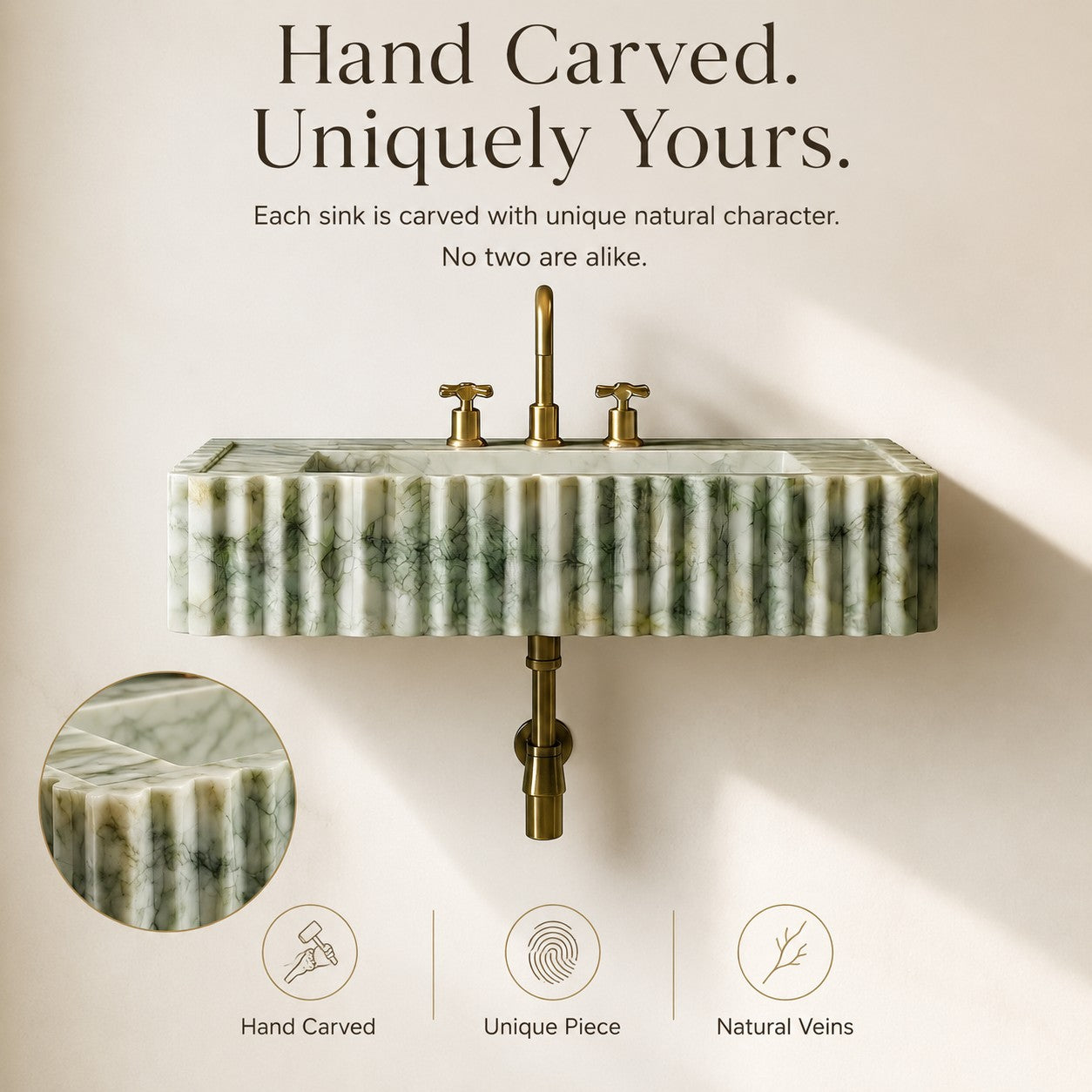 A wall-mounted sink made of carved green marble with natural veining and brushed brass hardware, shown against a warm beige wall with marketing text and a circular detail inset.