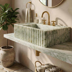 A rectangular marble sink with fluted vertical edges in white and pale green, mounted on a matching marble countertop with a gold faucet and gold wall hardware in a warm beige bathroom setting.