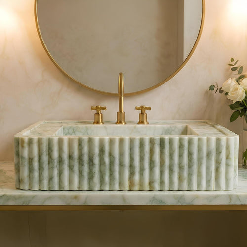 Marble sink with gold fixtures and a round mirror on a beige wall.