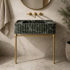 Green Levanto marble sink on brass console legs next to a glass shower