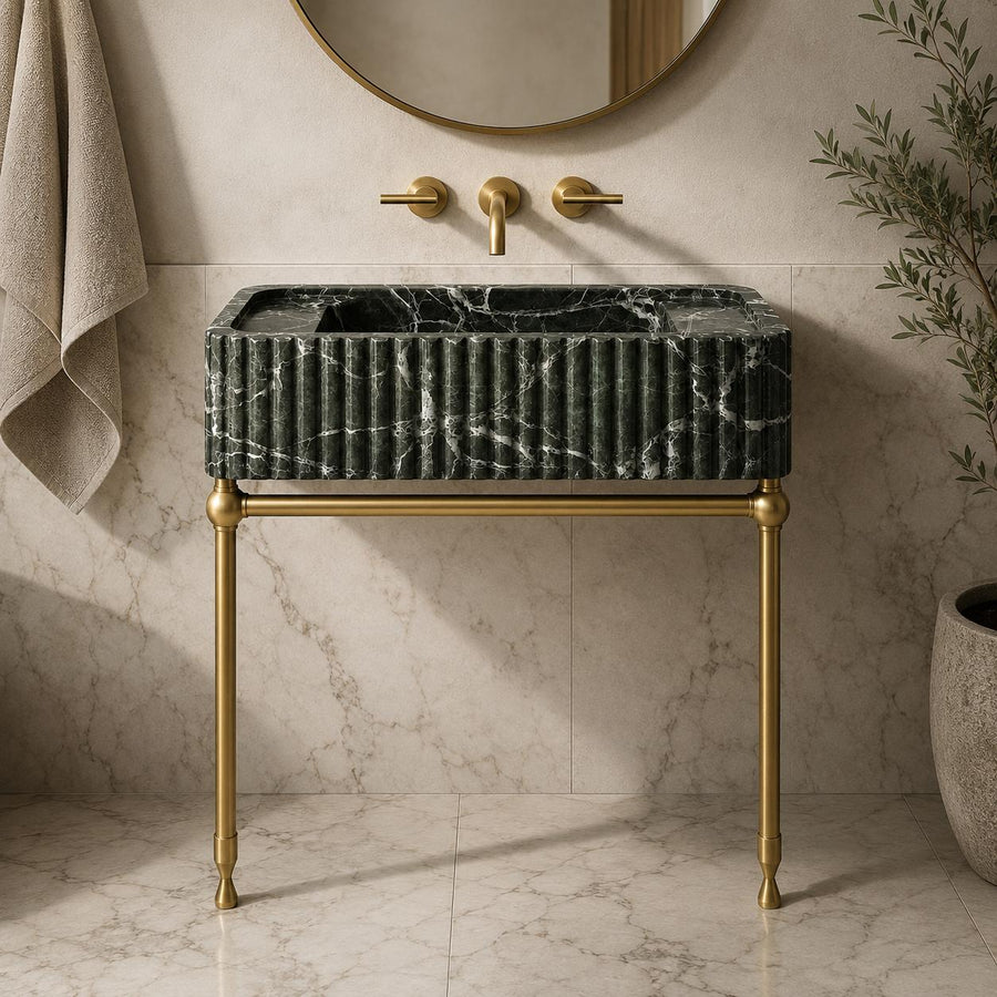 Green Levanto marble sink on brass console legs next to a glass shower