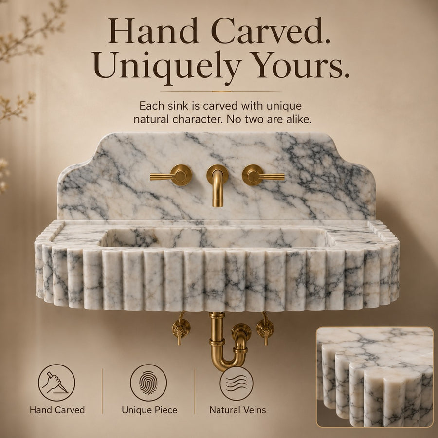 A hand-carved marble wall sink with a fluted front, brass faucet and handles, and exposed brass drain hardware, shown against a warm beige background with marketing text and feature icons.