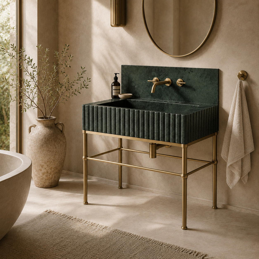 A modern bathroom vanity with a ribbed dark green rectangular sink top and a brass metal stand, set in a warm beige-toned bathroom with a round mirror, towel, and vase.