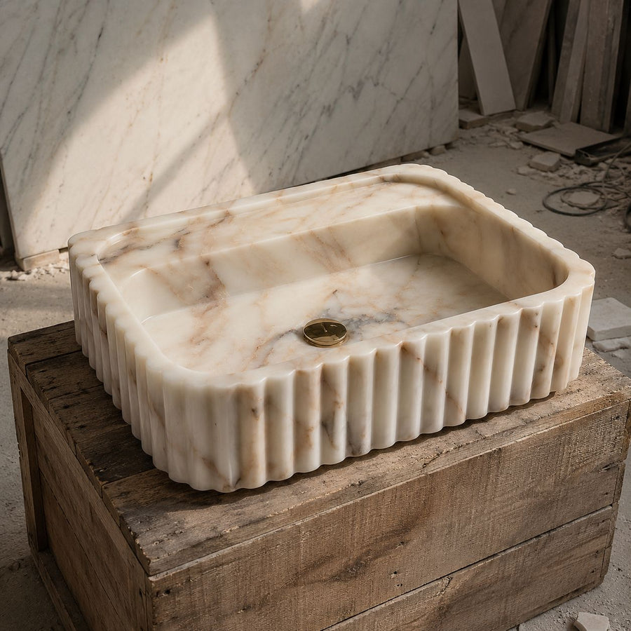 Handcrafted Calacatta Gold marble sink with fluted sides shown in a stone workshop