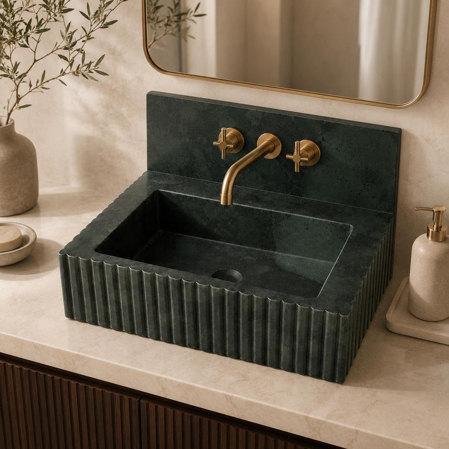 Green marble fluted sink with brass faucet and cross handles mounted on the stone backsplash