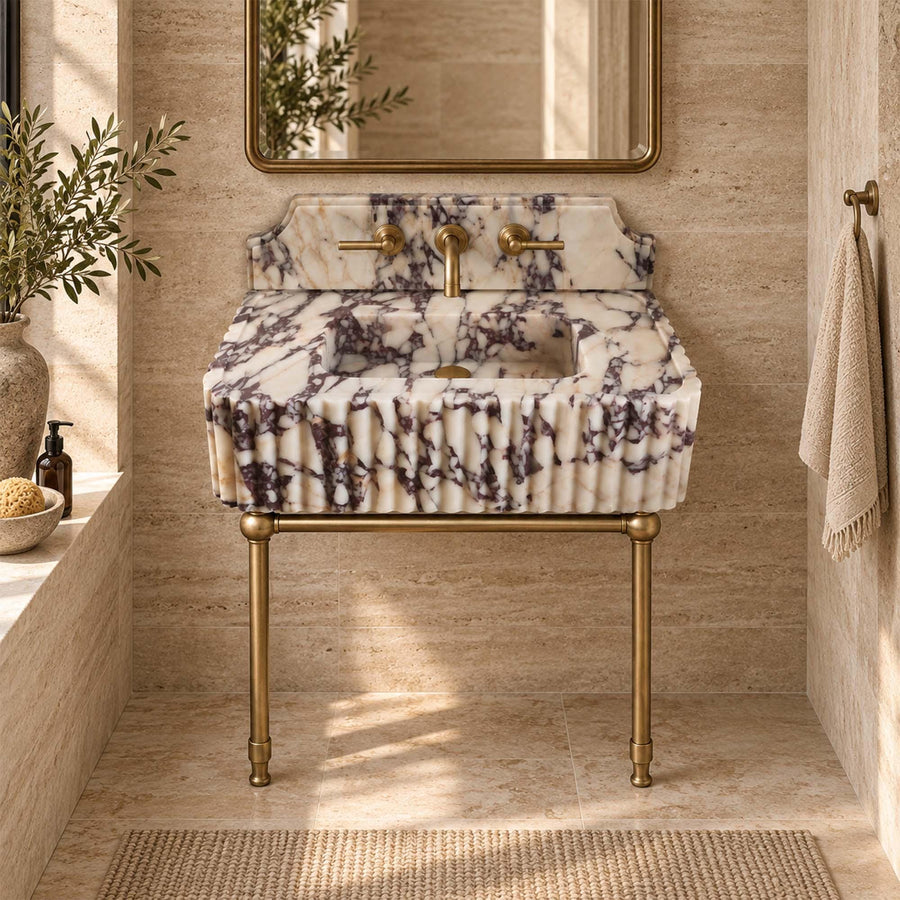 Calacatta Viola fluted marble vanity sink on slender brass legs, wall-mounted brass faucet in a bathroom