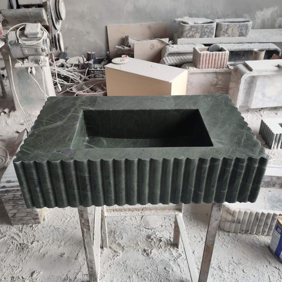 Floating green marble fluted sink with wide stone deck and brass wall-mounted faucet in a bathroom